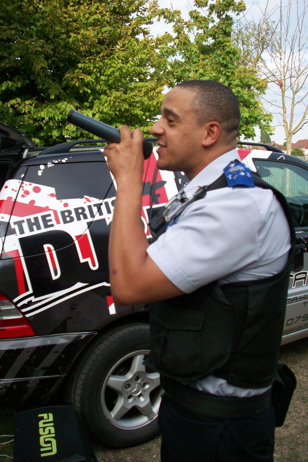 MC hosting on the mic beside the branded DJ vehicle at a community event