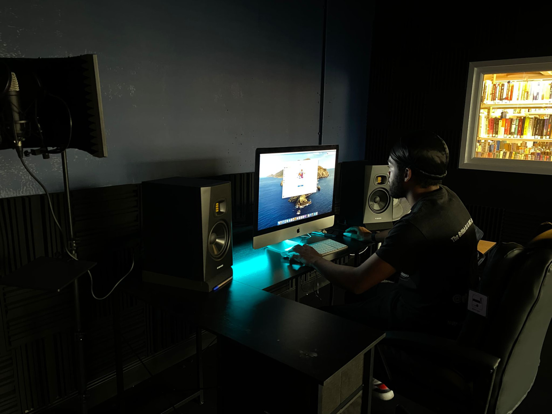Producer working at the studio iMac under teal desk lighting